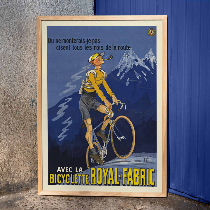 Michel Liebeaux Royal-Fabric bicycle poster with cyclist riding uphill in yellow gear against a moody blue mountain sky, framed and displayed in home decor