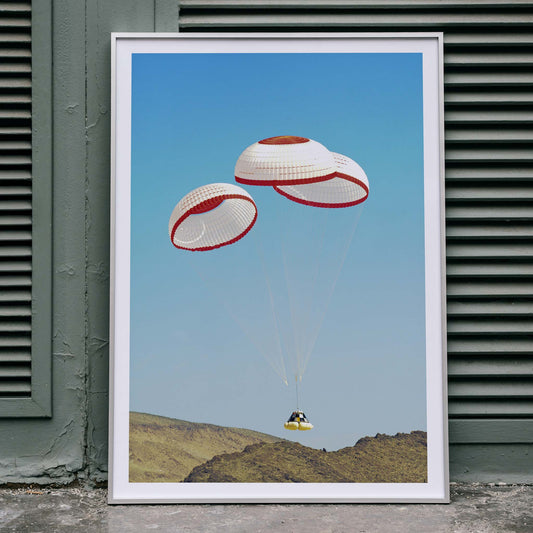 CST-100 crew capsule landing with three parachutes over desert landscape by NASA and The Boeing Company poster artwork, framed and displayed in home decor
