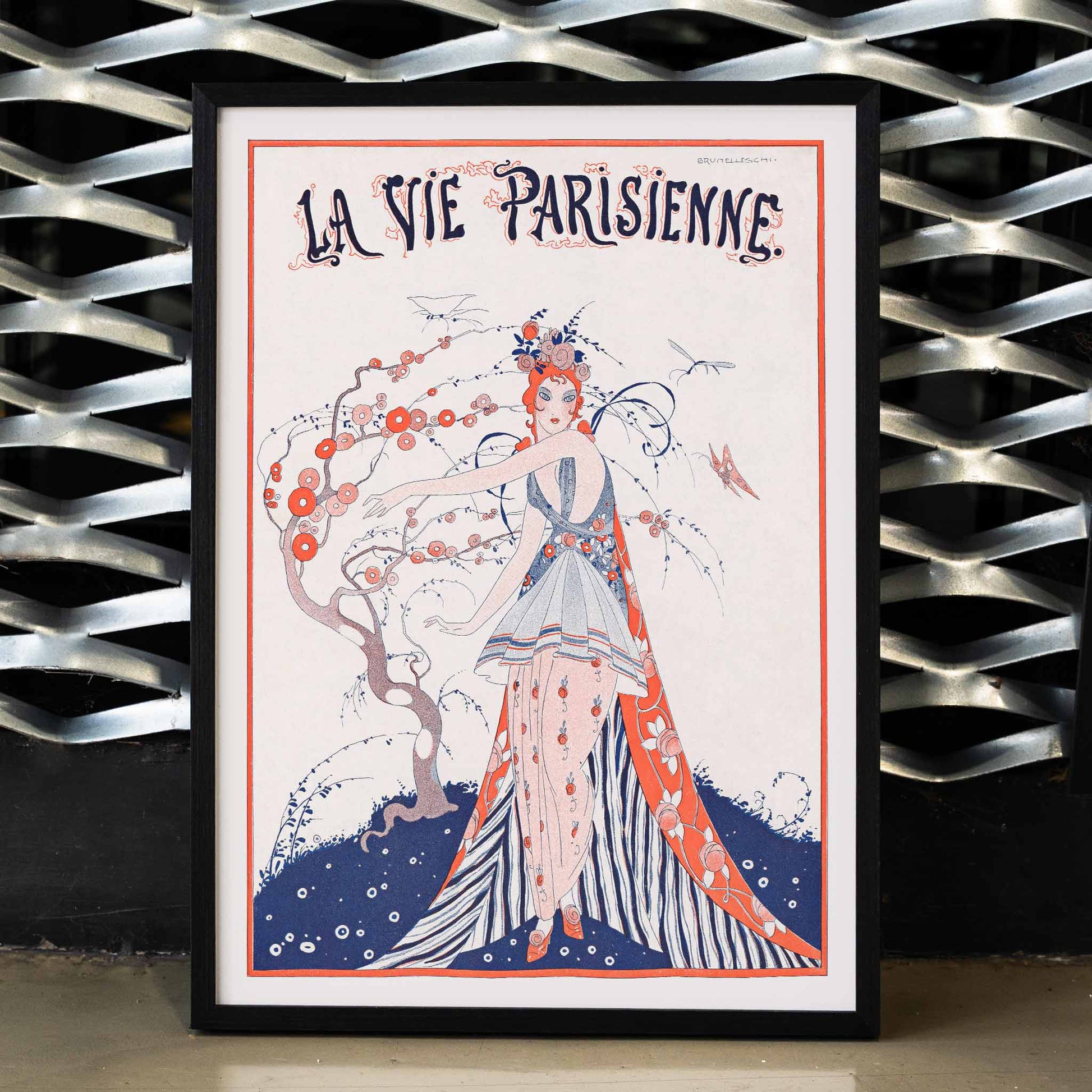 Elegant Art Deco poster of a woman in a floral dress standing by a blossoming tree La Vie Parisienne by Umberto Brunelleschi, framed and displayed in modern living room decor
