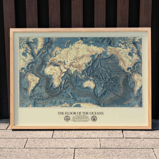 World map artwork showing ocean floors titled The Floor of the Oceans bathymetric map poster, framed and displayed in home decor