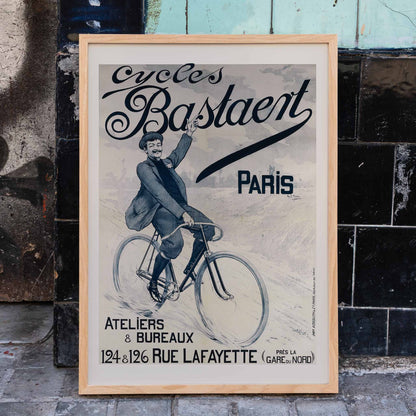Vintage bicycle poster joyful man riding and waving on Cycles Bastaent Paris bike artwork by Charles Tichon, framed and displayed in home decor