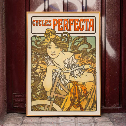 Art Nouveau poster of a woman with flowing hair riding a bicycle with decorative floral design by Alphonse Mucha for Cycles Perfecta, framed and displayed in home decor