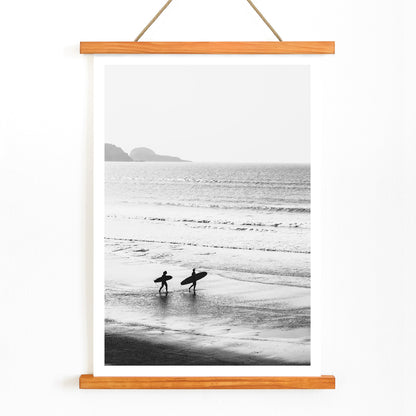 Black and white poster of surfers walking along the beach Surfers walking on the beach artwork, with wooden magnetic frame on white background