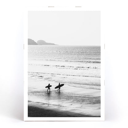 Black and white poster of surfers walking along the beach Surfers walking on the beach artwork, framed and displayed in modern living room decor