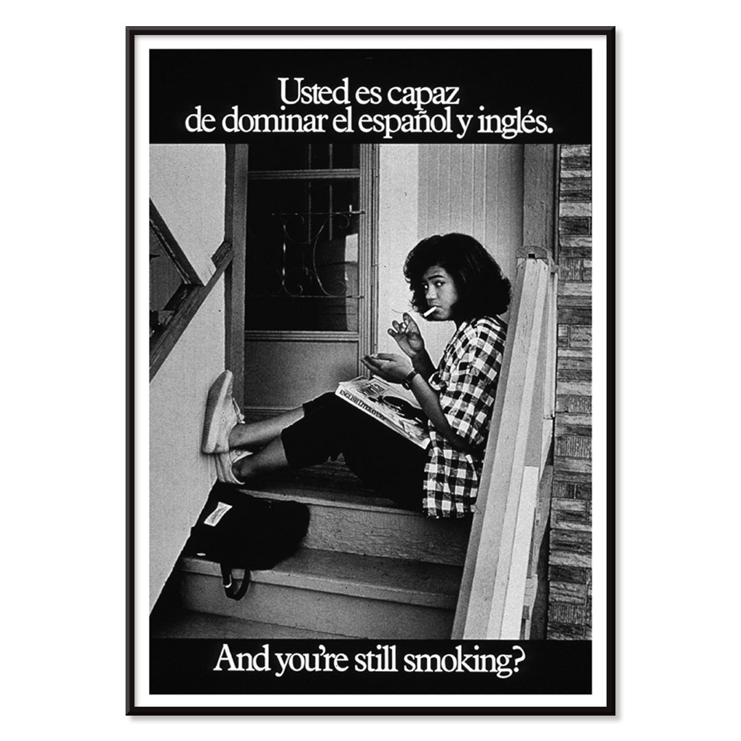 Young woman reading and smoking on stairs in bilingual anti-smoking poster by US Department of Health and Human Services titled Usted es capaz de dominar el español y inglés and you are still smoking, with black aluminium frame on white background